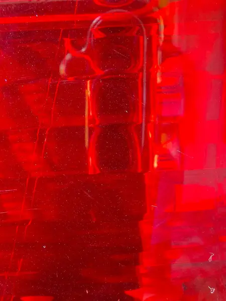 Parlak yansımaları ve dikey doğrusal desenleri olan yarı saydam kırmızı bir yüzeye yakın çekim, dinamik hareketi ve canlı renklerde görsel derinliği çağrıştırır..