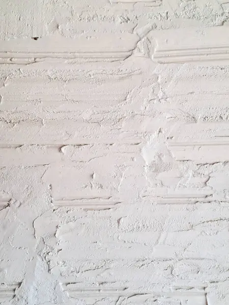 Beyaz alçıyla kaplanmış, yatay tuğla hatları ve düzensiz alçı kaplamayla kaplanmış, rustik kabartma ve doku oluşturan tuğla bir duvarın yakın plan görüntüsü. Olukların, havan ve küçük kusurların ayrıntıları yüzeye eski, el yapımı bir uygulama verir.