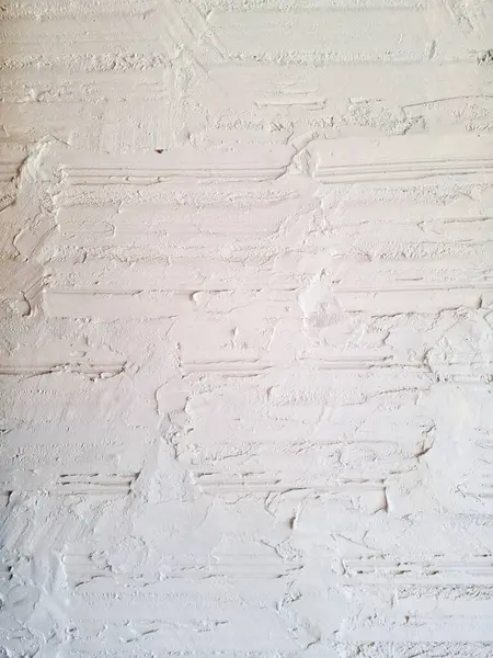 Beyaz alçıyla kaplanmış tuğla bir duvarın yakın plan görüntüsü, tuğlaların üzerinde bir malanın oluşturduğu belirgin yatay oyuklar içeriyor. Yüzeyde düzensiz kabartmalar, oyuklar ve kusurlar sergilenir. Bu da kırsal, el yapımı bir görünüm sağlar.