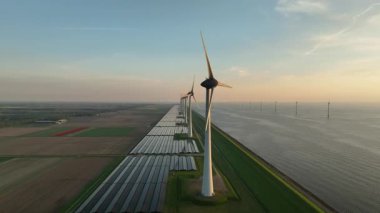 Bir göl kıyısındaki rüzgar türbinleri ve güneş panelleri yukarıdan görülen bahar günbatımında sürdürülebilir enerji üretiyorlar..