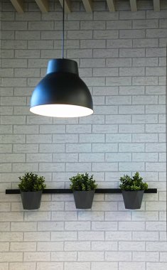 Büyük, koyu gri abajurlu parlak bir iç mekan ve duvarda gri kaplarda yeşil bitkiler asılı.