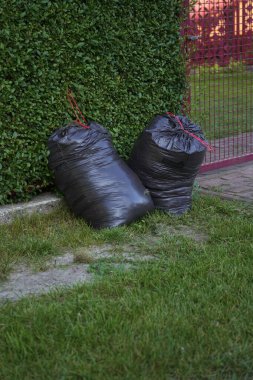 Yeşil bir çite karşı iki büyük siyah çöp torbası..