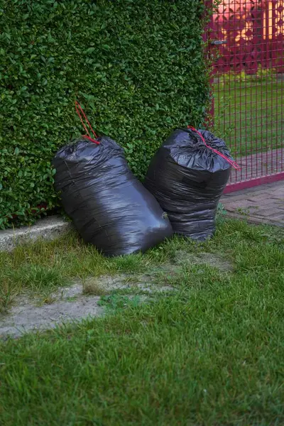 Yeşil bir çite karşı iki büyük siyah çöp torbası..