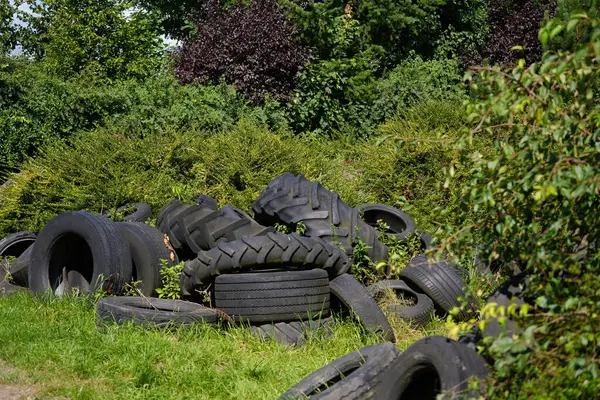 Yeşil doğaya karşı eski araba ve traktör lastikleri yığını.