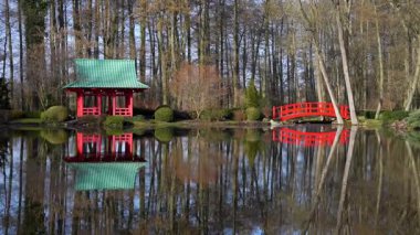Kırmızı çardak ve kırmızı köprü Japon usulü Bahar bahçesinde bir gölün kıyısında