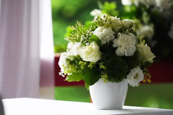 Beyaz gül buketi ve yeşil arka planda beyaz vazoda dekoratif yeşille karanfiller.