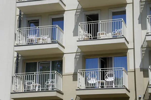 Balkonlu çok katlı bir bina, her balkonun beyaz bir masası ve iki beyaz sandalyesi var..