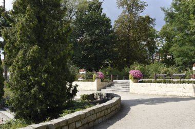 The park with a stone wall, pathway, benches, and flowers creates a sense of calm and relaxation