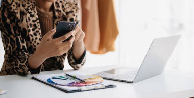 Sakin kıvırcık esmer, esmer kadın moda tasarımcısının ofisinde ve elinde tablet ve akıllı telefon var.