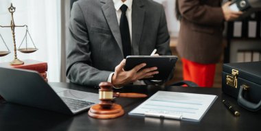 Adalet ve hukuk kavramı. Hukuk temalı ahşap masa, kitaplar, denge. Tokmak, mahkeme salonunda dijital tablet bilgisayarla çalışan bir erkek yargıç.