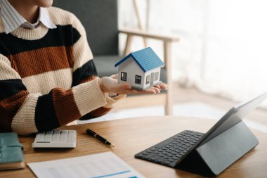 Ev modeli emlakçı ve müşteriyle birlikte çalışan Asyalı bir kadın ev, sigorta veya kredi emlak danışmanlığı için ev kredisi teklifiyle ilgili sözleşme üzerinde tartışıyorlar.