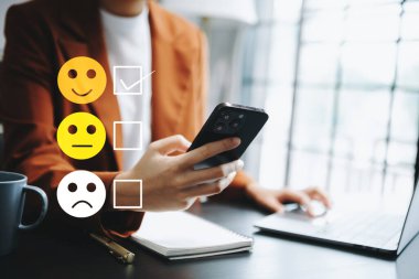 Müşteri hizmetleri değerlendirme konsepti. Kadın gülümseme ifadelerini sanal ekranda göster. Akıllı telefon ve laptoya bakıyor.