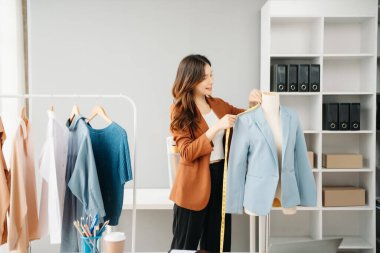 Başarılı bir moda tasarımcısı. Atölyede dururken gülümseyen çekici Asyalı kadın. Güzel iş kadını çalışıyor ve stüdyoda tablet, laptop ve akıllı telefonu tutuyor..