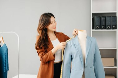 Başarılı bir moda tasarımcısı. Atölyede dururken gülümseyen çekici Asyalı kadın. Güzel iş kadını çalışıyor ve stüdyoda tablet, laptop ve akıllı telefonu tutuyor..