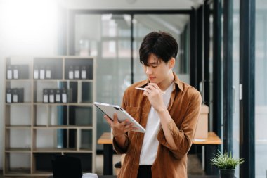 Modern ofiste laptopla, tabletle çalışan ve kağıda not alan genç bir iş adamı.. 