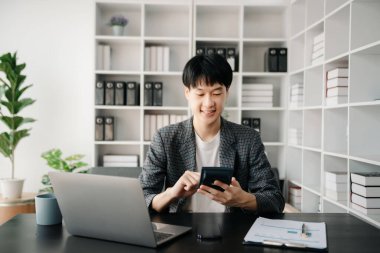 Ofisteki masasında oturan Asyalı genç adamın portresi.