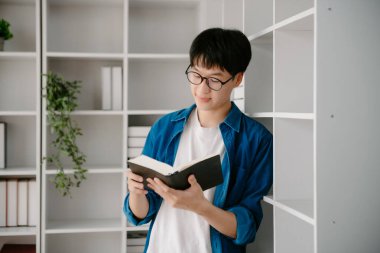 Erkek öğrenciler, Asyalı adam kütüphanesindeki kitaplardan dizüstü bilgisayar ve tablet kullanarak online bilgileri araştırıyorlar.
