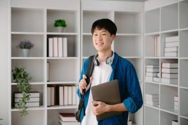 Erkek öğrenciler, Asyalı adam kütüphanesindeki kitaplardan dizüstü bilgisayar ve tablet kullanarak online bilgileri araştırıyorlar.