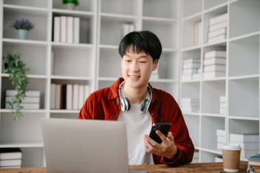 Mutlu Asyalı iş adamı modern ofiste akıllı telefondan, tabletten ve laptoptan konuşma zevkine sahip. 