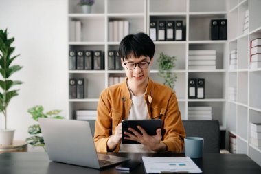 Ofisteki masasında oturan Asyalı genç adamın portresi.