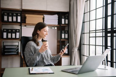 İş kadını telefonda konuşuyor ve evde otururken gülümseyen bir laptop kullanıyor.