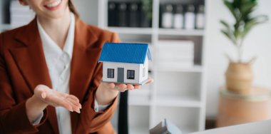 Genç emlakçı Laptop ve tabletle modern ofiste ve yanında küçük bir evde çalışıyor.