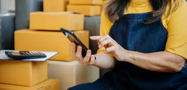 Olgun iş sahibi kadın paket kutusunu hazırla ve tablet, dizüstü bilgisayar alışverişi online konsept üzerinden müşteriye teslimat için çevrimiçi kontrol yap