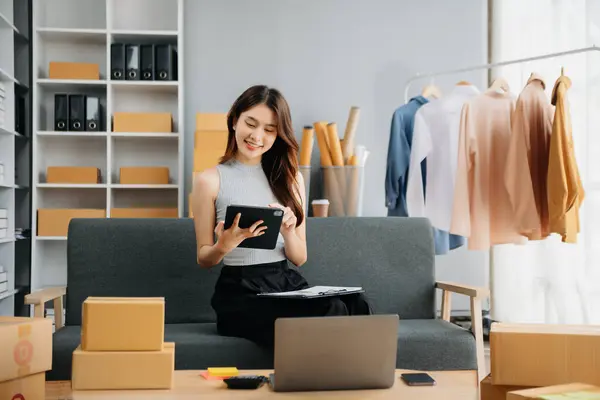 Çevrimiçi mağaza işleten genç kadın akıllı telefon ya da tablet kullanarak küçük işletme KOBİ 'si başlat, çevrimiçi satın alma oranları al ve kontrol et