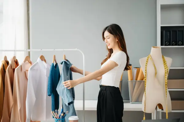 Başarılı bir moda tasarımcısı. Atölyede dururken gülümseyen çekici Asyalı kadın. Güzel iş kadını çalışıyor ve stüdyoda tablet, laptop ve akıllı telefonu tutuyor..