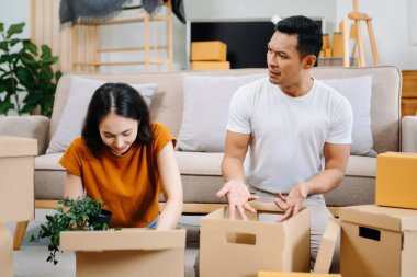 Büyük kutuları olan genç bir çift yeni bir eve taşınıyor, çift için yeni bir daire, genç Asyalı erkek ve kadın yeni ev için kanepenin taşınmasına yardım ediyorlar.