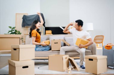 Büyük kutuları olan genç bir çift yeni bir eve taşınıyor, çift için yeni bir daire, genç Asyalı erkek ve kadın yeni ev için kanepenin taşınmasına yardım ediyorlar.