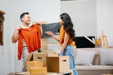 Asyalı genç ve çekici çift, yeni eve taşınmak için tablet ve akıllı telefon kullanıyor. Alışveriş mobilyaları, karton paketlerle dekore ediliyor.. 