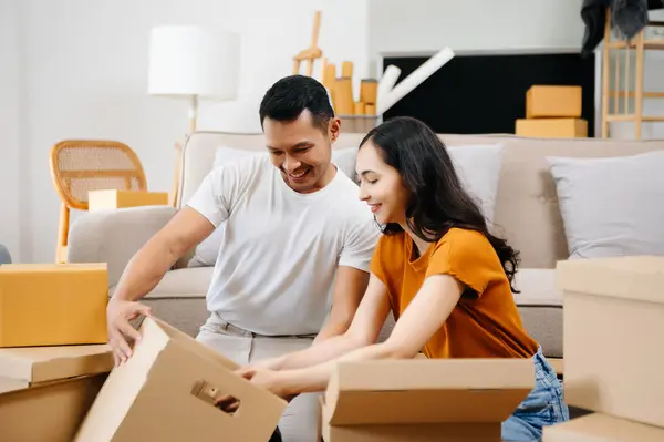 Asyalı genç ve çekici çift, yeni eve taşınmak için tablet ve akıllı telefon kullanıyor. Alışveriş mobilyaları, karton paketlerle dekore ediliyor.. 
