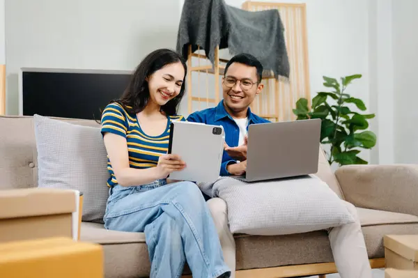 Asyalı genç ve çekici bir çift, yeni evlerinde tablet ve akıllı telefon, alışveriş mobilyaları, karton paketlerle dekore edilmiş evler kullanıyor. Genç evli Asyalı eve taşınıyor..