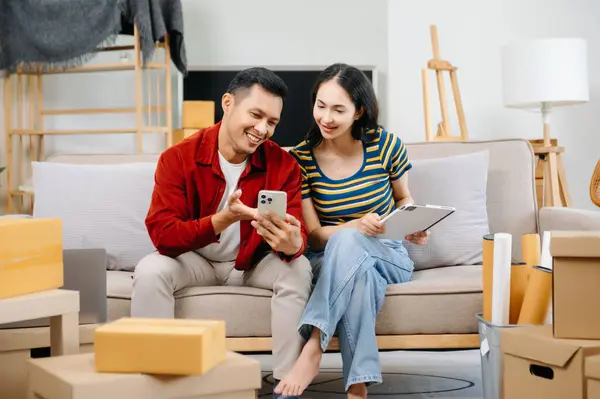 Asyalı genç ve çekici bir çift, yeni evlerinde tablet ve akıllı telefon, alışveriş mobilyaları, karton paketlerle dekore edilmiş evler kullanıyor. Genç evli Asyalı eve taşınıyor..