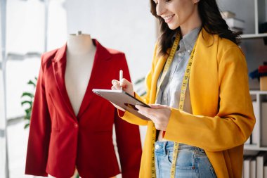Boyunlarında santimetre boyayla çalışan ve tablet ve akıllı telefon tutan çeşitli kadın moda tasarımcıları. bağımsız yaratıcı tasarım işi.