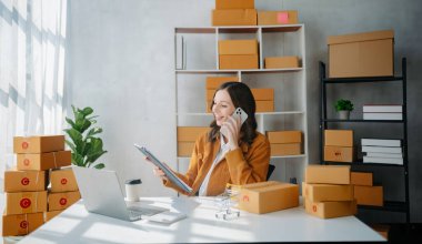 Genç işyeri sahibi kadın paket kutusu hazırlıyor ve tablet, dizüstü bilgisayar alışverişi online konsepti üzerinden müşteriye teslimat için çevrimiçi olarak kontrol ediliyor. ev ofisinde.