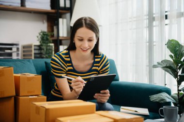 Beyaz kadın KOBİ akıllı telefon ya da tablet kullanarak çalışıyor online alışveriş siparişlerini alıyor ve kontrol ediyor, serbest iş çevrim içi konsepte