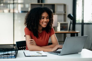 Tablet ve dizüstü bilgisayarda yazan genç bir kadın çalışan beyaz masada modern bir ofiste oturuyor.