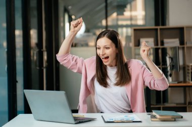 Kendine güvenen iş uzmanı, gülümseyen, dizüstü bilgisayarda yazan ve dijital tableti yaratıcı ofiste tutan çekici genç bir kadın.