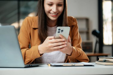 Kendine güvenen iş uzmanı, gülümseyen, dizüstü bilgisayarda yazan ve dijital tableti yaratıcı ofiste tutan çekici genç bir kadın.