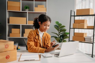 Genç Afrikalı kadın paket kutusunu hazırla ve tablet, dizüstü bilgisayar alışverişi online konsept üzerinden müşteriye teslimat için çevrimiçi kontrol yap