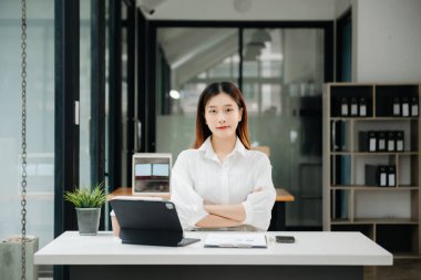 Çalışan not defteri, tablet ve laptop belgeleriyle modern ofiste çalışan Asyalı iş kadını.