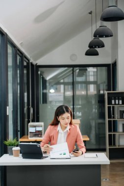 Tablet ve dizüstü bilgisayarda yazan genç ve güzel bir kadın beyaz çalışma masasında oturuyor.