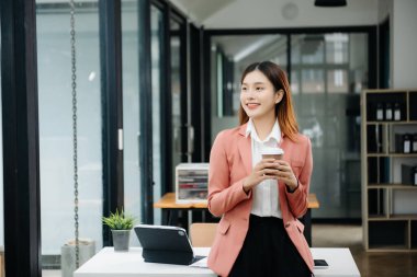 Tablet ve dizüstü bilgisayarda yazan genç ve güzel bir kadın beyaz çalışma masasında oturuyor.