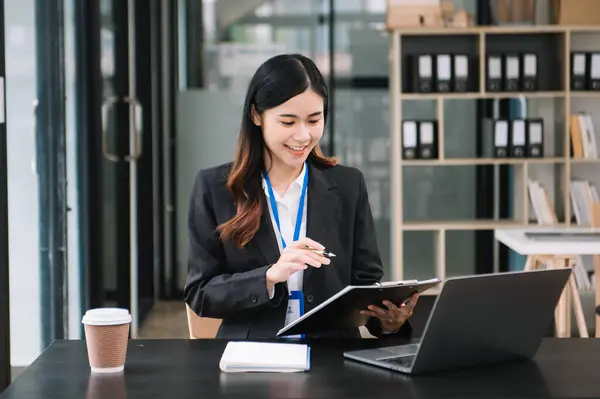 Kendine güvenen iş uzmanı çekici, gülümseyen genç bir kadın yaratıcı ofiste elinde dijital tablet tutuyor.