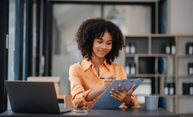 Confident business expert attractive smiling young woman typing laptop ang holding digital tablet  on desk in creative office