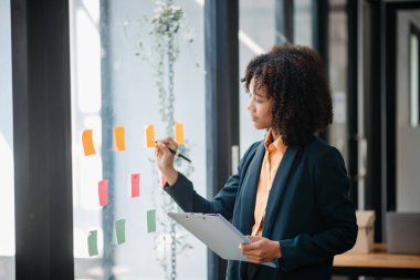 Gökdelendeki modern ofiste çalışan sekreter, pencere kenarındaki görevlere yapışkan notlar yazıp yapıştırıyor