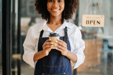 Kahve Dünyası Konsepti. Kameraya gülümseyen güzel bayan kahve dükkanında tek kullanımlık kahve ikram ediyor.