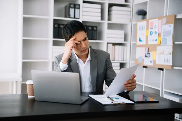 Asyalı iş adamı, ofisteki tablet üzerinde çalıştığı için stresli, sıkılmış ve çok fazla düşünüyor.